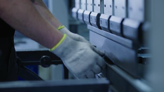 Tracking shot of gloved worker feeding and bending metal sheet on press brake in industrial factory workshop.