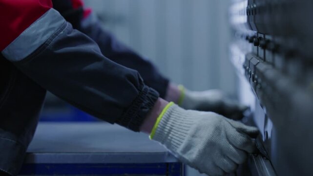Tracking shot of worker aligning metal sheet on press brake in industrial workshop.