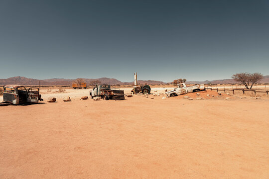 View of sun-bleached, decaying vehicles rest in the stark desert landscape under a vast, cloudless sky, evoking desolation, Namibia, Africa, Namibia.