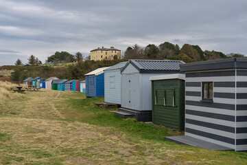 Obraz premium Hopeman beach huts line a coastal path under a cloudy Scottish sky, with a grand building visible on the distant hill