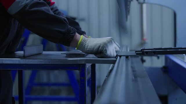 Slow motion gloved worker feeding flat metal sheet into hydraulic press on steel fabrication bench inside industrial workshop. tracking shot.
