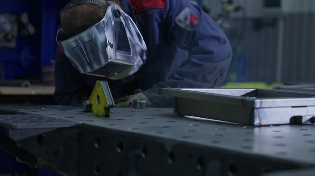 Slow motion welder welding steel frame on metal workbench in industrial workshop, tracking shot.