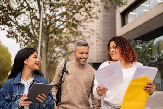 Multiethnic friends walking in city sharing documents