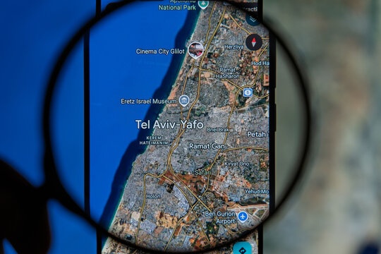 Magnifying glass over a smartphone screen displaying a digital map of Tel Aviv Yafo, highlighting urban areas, roads, and Ben Gurion Airport for travel and navigation concepts 
