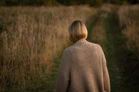 Woman in knitted sweater walking through autumn field