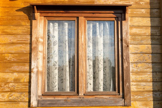 Wooden window with floral curtains in sunlight