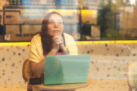 A woman thoughtfully sits in front of her laptop