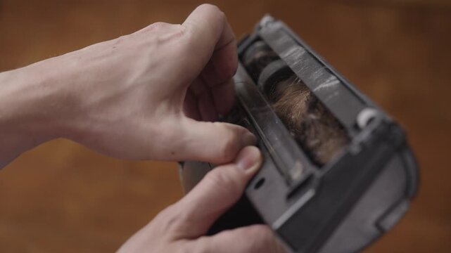Close-up of person inspecting vacuum cleaner brush roller clogged with hair and dust, performing necessary maintenance and cleaning of appliance to ensure effective operation and cleanliness.