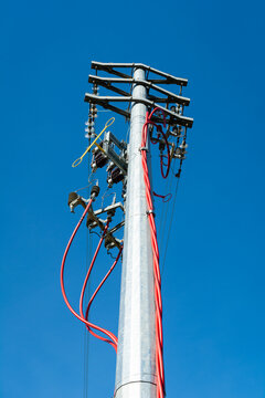 View of a tall, silver utility pole with vibrant red cables stretching against a clear blue sky, Pontremoli, Tuscany, Italy.