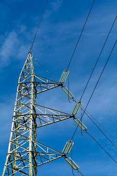 View of a towering metal lattice structure of an electricity pylon reaching towards the bright blue sky, with its cables stretched, Pontremoli, Tuscany, Italy.