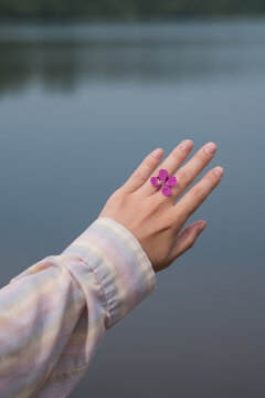 Hand with fireweed flower in focus near lake
