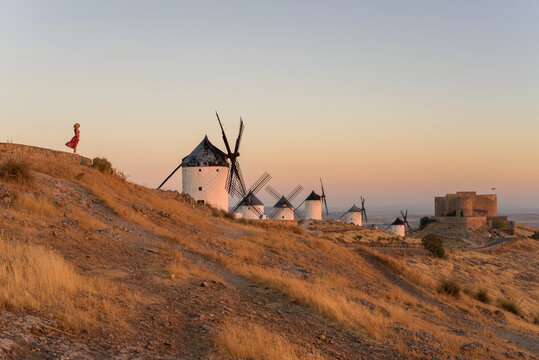 Woman exploring Consuegra at sunset with windmills
