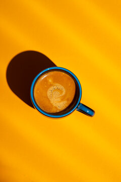 Top view of coffee in blue mug on yellow background