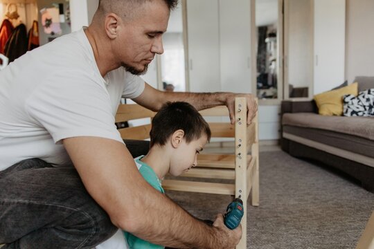Father and son assembling a wooden baby cot together