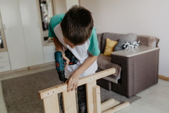 Young boy assembling wooden baby cot with power drill