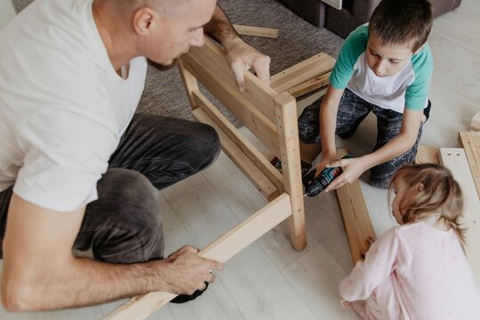 Father assembling baby cot with children