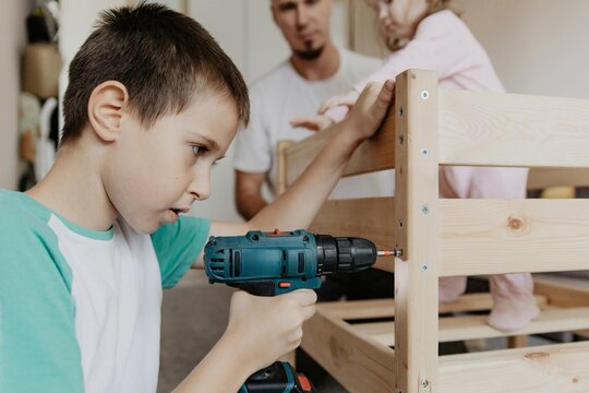 Young boy uses drill to build a wooden baby cot