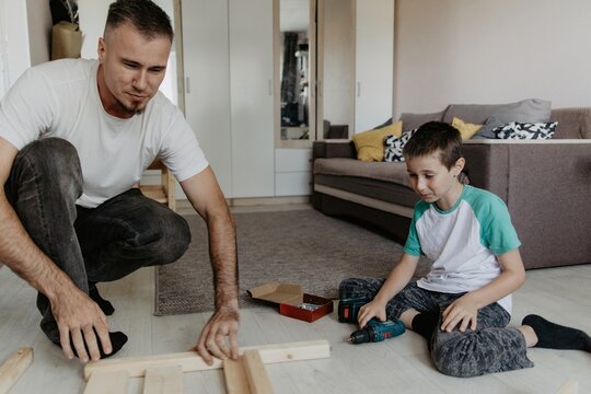 Father and son assembling wooden baby cot together