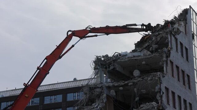 A giant demolition crane tears down an office building piece by piece, its powerful claw gripping and dismantling each section with force.
