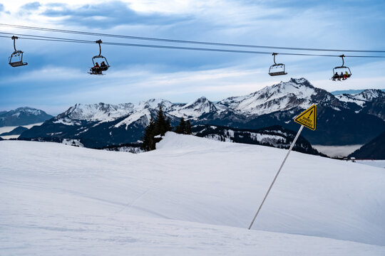 View of chairlifts glide above the snowy expanse, with the majestic, snow-capped mountains piercing the horizon, a warning sign stands vigil, Val-d'Illiez, Valais, Switzerland.
