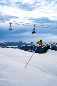 View of snow-covered slopes under a web of ski lifts against the backdrop of majestic mountains and a warning sign, Val-d'Illiez, Valais, Switzerland.