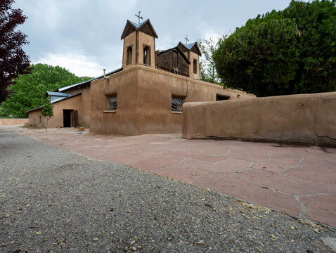View of the historic adobe architecture of the San Miguel Mission under a cloudy sky, its weathered walls telling tales of time, Santa Fe, New Mexico, United States.