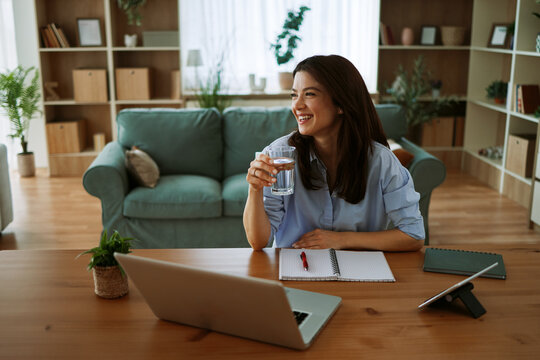 Young woman smiling while working from home holding a glass of water at her desk