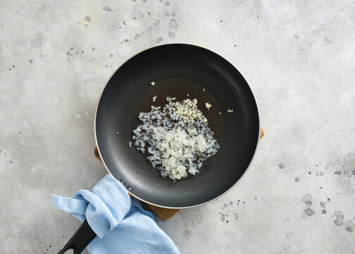 Cooking chopped onions and garlic in a frying pan on a kitchen counter at home in the afternoon