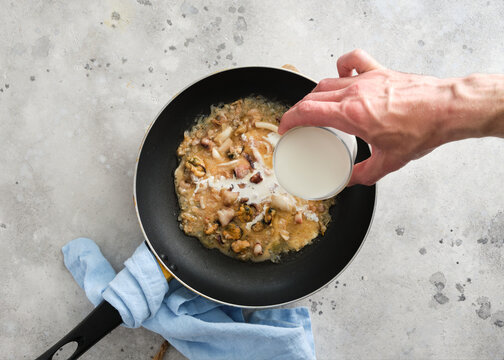 Cooking a dish with seafood and cream in a frying pan on a kitchen counter during the day