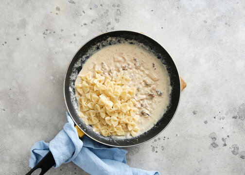 Cooking pasta in a skillet with creamy sauce and ingredients in a kitchen setting during daytime hours