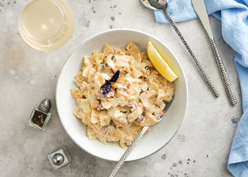 Creamy pasta dish served in a bowl with a slice of lemon and toppings on a light surface