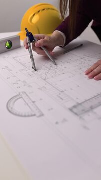 Close-up video of a female architect using a drafting compass and reviewing architectural blueprints on a desk with technical tools in an office workspace.