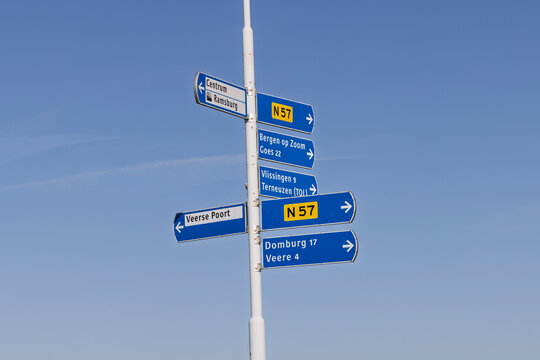 Middelburg, Zeeland, Netherlands. 18 March 2026. Blue Directional Road Signs on White Pole in Zeeland, Pointing to Domburg, Veere, Vlissingen and Goes under Clear Blue Sky.