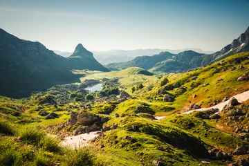 Rolling green hills and majestic cliffs under a clear blue sky at dawn. Location place Durmitor National park, Stozina peak, Montenegro, Europe. © Leonid Tit