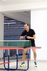 Fototapeta premium Ready stance of a male table tennis player in black shirt in gym.