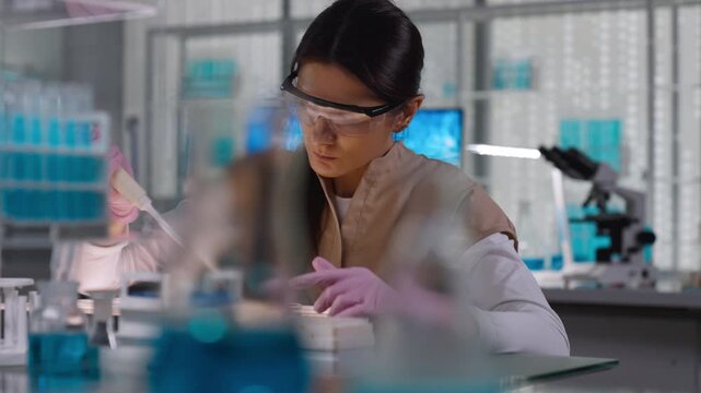 Female scientist in protective gear working in a modern laboratory to test blood samples. Preparing test samples with a pipette. Selective focus on the person