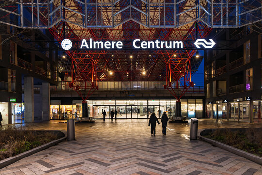 Almere, Netherlands. 14 March 2026. Modern Entrance of Almere Centrum Railway Station at Night with Illuminated Red Space Frame Roof, Digital Clock and Pedestrian Tunnel Access