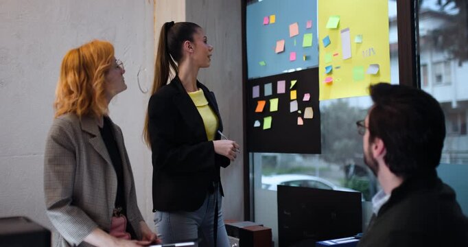 Presentation of ideas using sticky notes in an office setting with three people engaged in discussion during the daytime