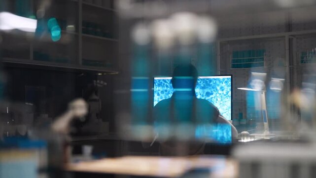 Female scientist in protective gear working in a modern laboratory to test DNA. Examining data on a computer. Selective focus on the person