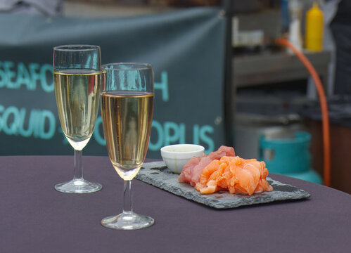 Two glasses of sparkling drink beside salmon and tuna sashimi at Prague Naplavka farmers market. Elegant street food scene combining seafood, leisure and weekend lifestyle.