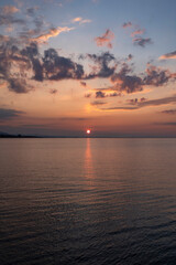 Obraz premium Breathtaking sunset over Lake Constance viewed from the Bregenz shore, featuring a vibrant orange sun dipping towards the horizon with dramatic clouds reflecting in the calm water.