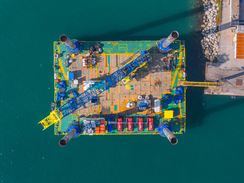 Aerial view of a platform with a crane and containers casting long shadows onto the shimmering turquoise water near the harbor, Ortona, Abruzzo, Italy.