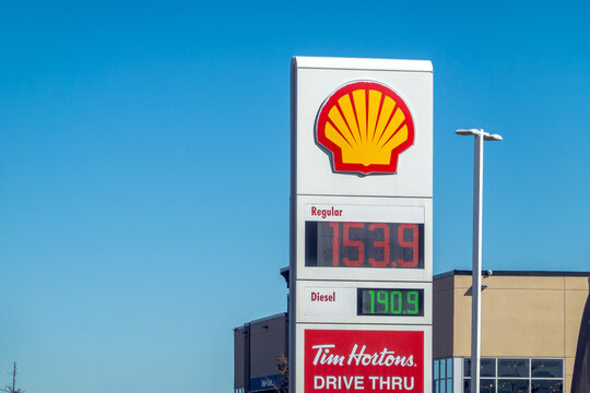 Calgary, Alberta, Canada. March 23, 2026. A Shell gas station sign displaying fuel prices and a Tim Hortons drive-thru logo against a clear blue sky.