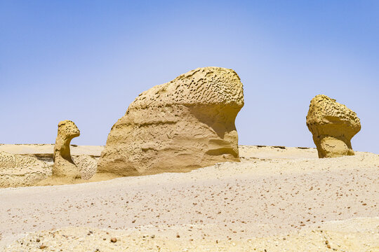 View of weathered rock formations stand as silent sentinels against the stark blue sky, sculpted by time and wind in Faiyum Governorate, Egypt.