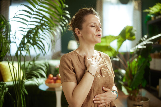 A woman practices deep, diaphragmatic breathing with her hands on her chest and stomach, fostering inner peace and stress relief in her comfortable living room.