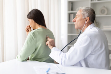 Fototapeta premium Doctor examining female patients lungs with stethoscope during medical checkup in clinic. Healthcare professional listening to breathing and evaluating respiratory health