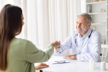 Obraz premium Senior male doctor greeting female patient with friendly fist bump during consultation. Medical professional building trust and positive relationship in healthcare environment