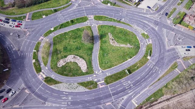 Drone aerial view of a large multi-lane roundabout with flowing traffic and road markings in Basingstoke, United Kingdom. Urban transport infrastructure with cars navigating junction and green central