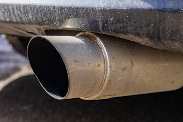 A car's exhaust pipe is dirty and has buildup. This is seen in a parking lot under natural light