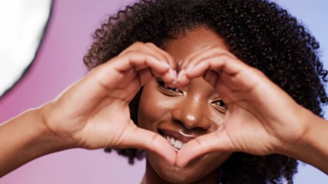 A woman making a heart shape with her hands over her face smiling